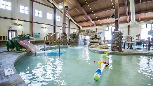 Piscina interior con una escultura de rana, un tobogán acuático y una pequeña embarcación.