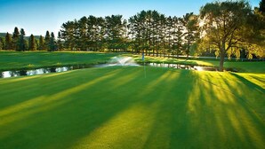 Un campo de golf con un estanque, árboles y cielo despejado.