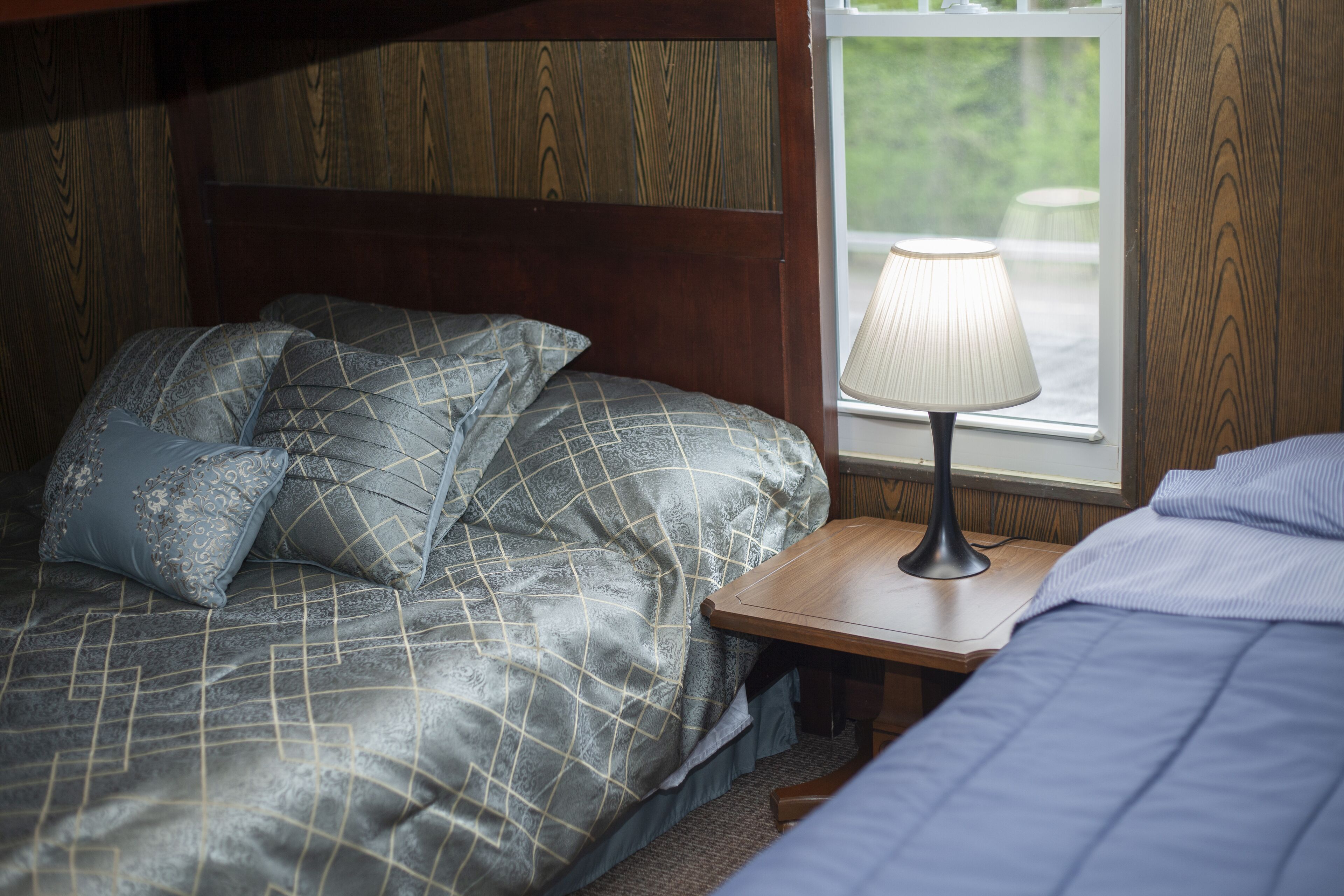 A bedroom with a bed, pillows, a nightstand, a lamp, and a window.