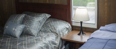 A bedroom with a bed, pillows, a nightstand, a lamp, and a window.