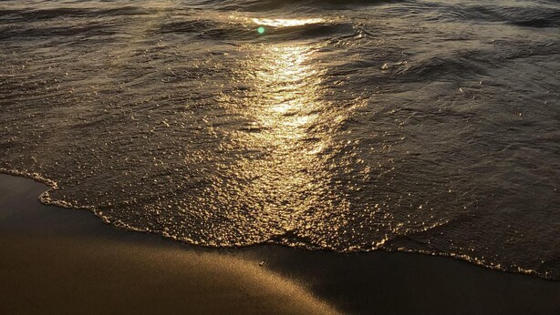 En strandscene med solnedgang over havet, bølger der forsigtigt slår mod kysten.