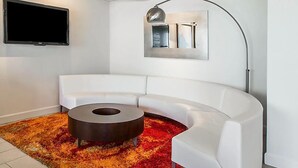 Una sala de estar moderna con un sofá seccional blanco, una mesa redonda de centro, un televisor de pantalla plana montado en la pared y una lámpara de pie.