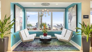 Un vestíbulo moderno con dos sillones blancos, una mesa redonda para café y un ventanal con vistas a palmeras y edificios.