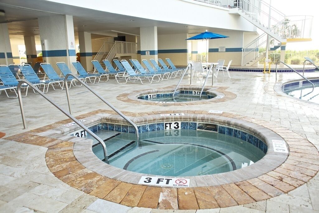 A swimming pool area with multiple hot tubs, lounge chairs, and a no diving sign.