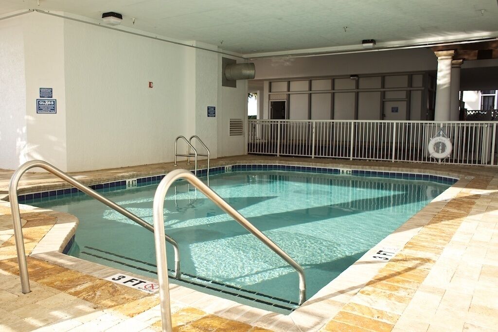 An indoor swimming pool with clear water, a 3 FT depth sign, and a white tiled floor.