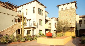 A multi-story hotel with a stone facade, balconies, and a courtyard with desert plants. - UpScale Resort with Outdoor Heated Pool with a waterslide and a poolside bar, tennis court and gym (Peoria)