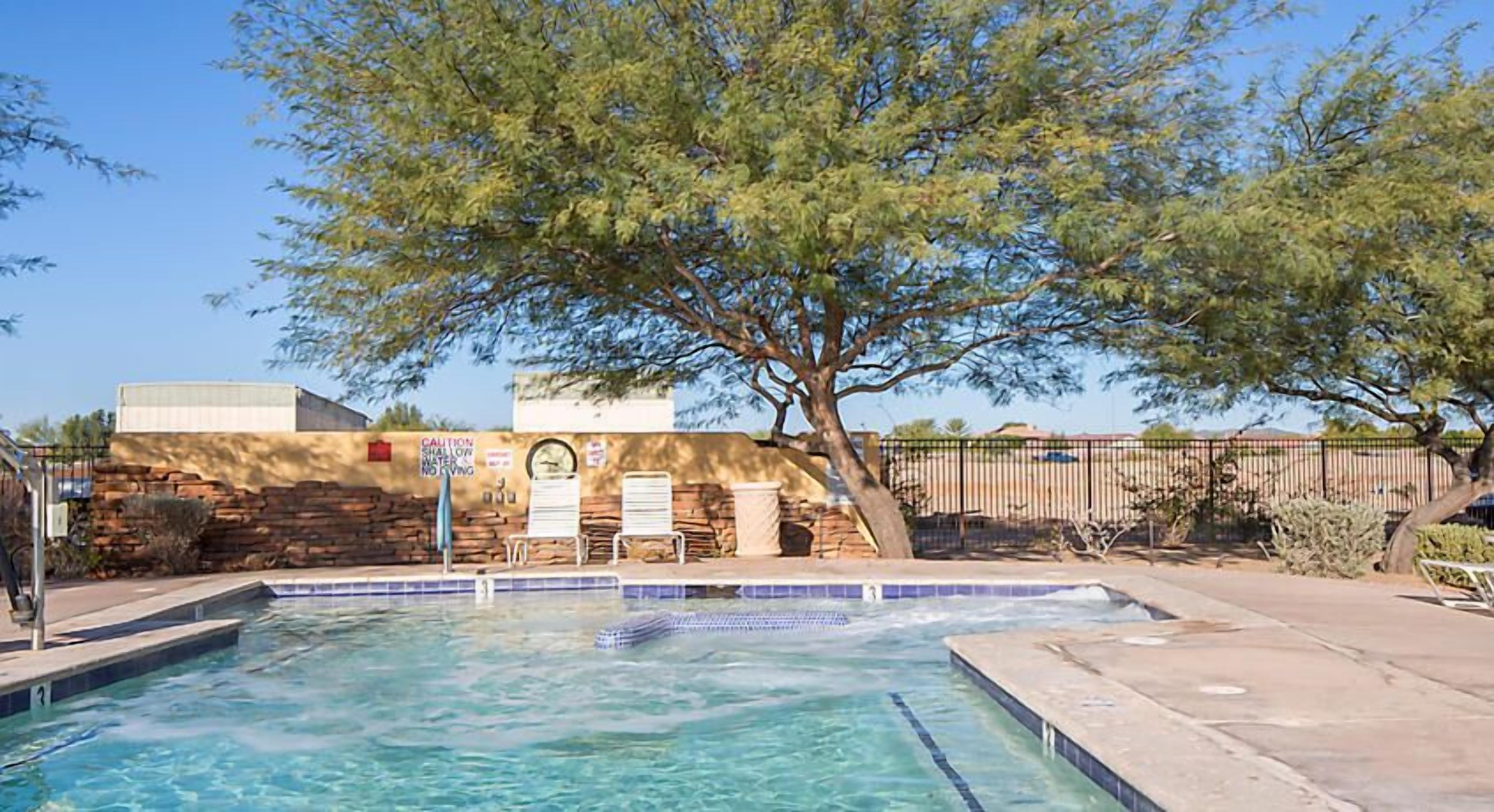 A swimming pool with a stone wall, a tree, and a caution sign.