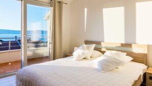 A bedroom with a large bed, a wooden headboard, and a view of the sea through a sliding glass door.