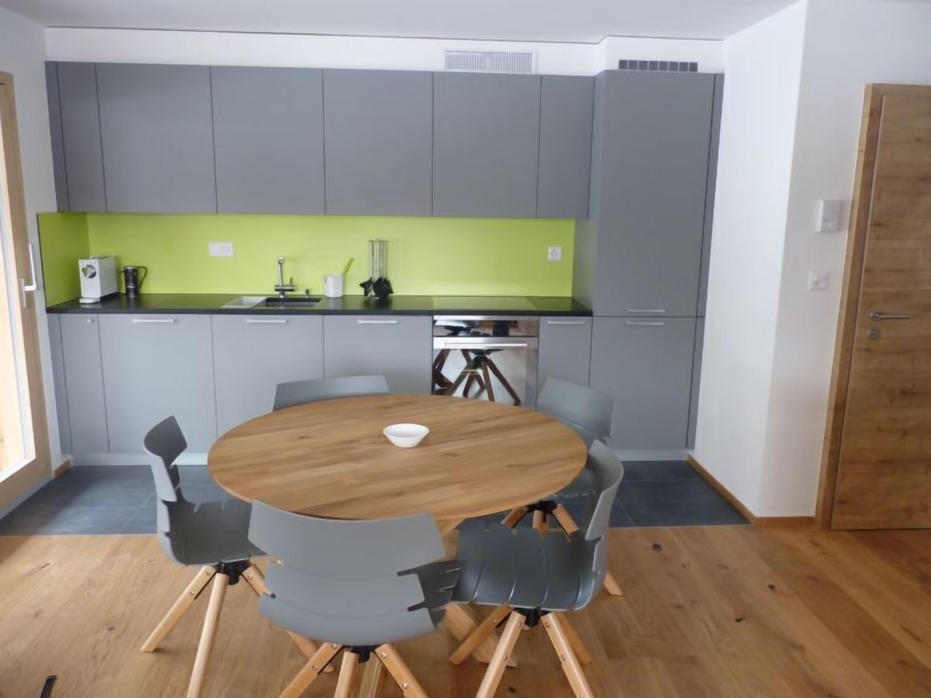Una cocina compacta con armarios grises, una encimera verde y una mesa de comedor de madera con cuatro sillas.