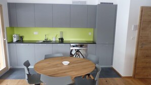 Eine kompakte Küche mit grauen Schränken, einer grünen Arbeitsplatte und einem Holzespeisetisch mit vier Stühlen.