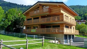 Ein mehrstöckiges Holzgebäude mit Balkonen, umgeben von einer Rasenfläche und Bäumen.