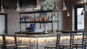 A bar area with a wooden counter, multiple shelves of bottles, and hanging pendant lights. - Ascent ON Main (PARKER)