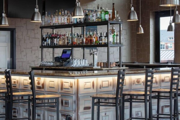 A bar area with a wooden counter, multiple shelves of bottles, and hanging pendant lights. - Ascent ON Main (PARKER)