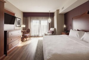 Habitación de hotel con una cama grande, un escritorio, una silla, un televisor y una ventana con cortinas.
