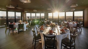 A restaurant with round tables set for dining, large windows offering a view, and pendant lighting. - Ascent ON Main (PARKER)