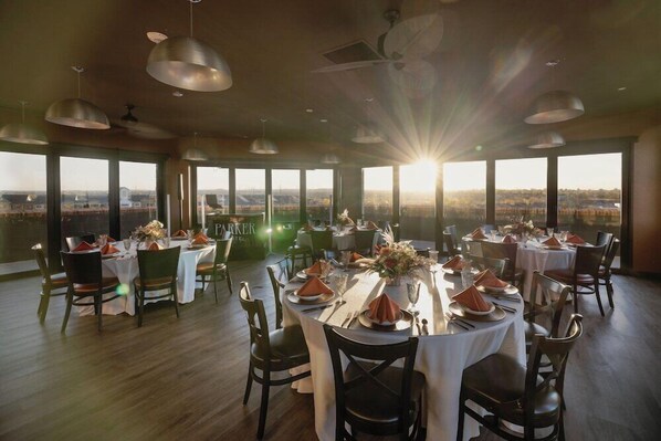 Ein Restaurant mit runden Tischen, großen Fenstern mit Blick und Pendelleuchten.