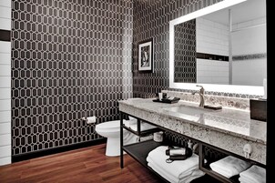 Un baño moderno con pared de diseño geométrico, un espejo grande, encimera de mármol y un inodoro.