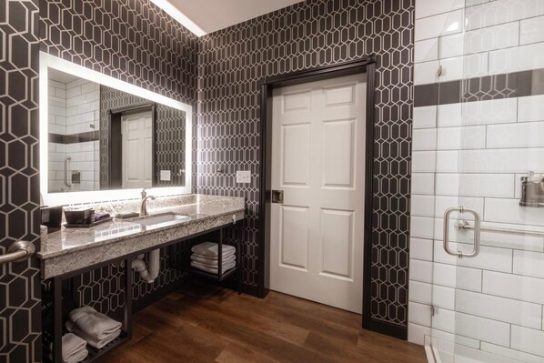 A modern bathroom with a large mirror, a sink, and a shower area. - Ascent ON Main (PARKER)