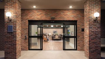 A brick-walled entrance with a glass door, a reception desk, and a seating area with a sofa and table.
