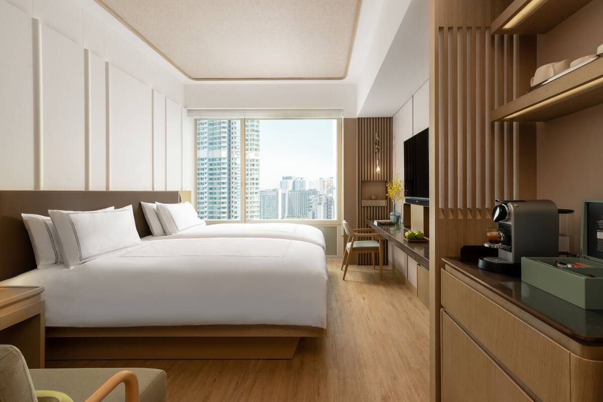 Een moderne hotelkamer met een groot bed, een bureau met een koffiezetapparaat, een televisie en uitzicht op de stad.