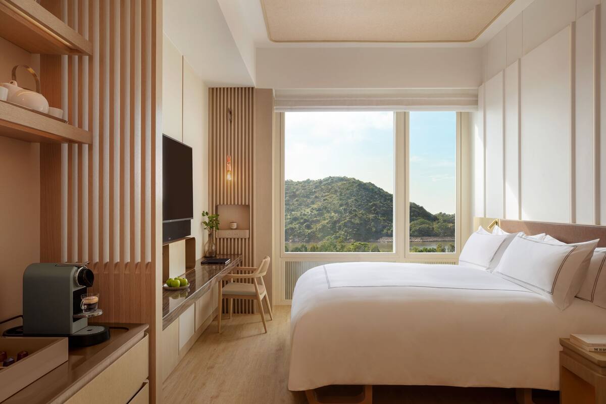 Hotelkamer met een groot bed, een bureau met een koffieapparaat, een televisie en uitzicht op een berg.