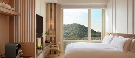 Habitación de hotel con una cama grande, un escritorio con cafetera, televisión y vistas a la montaña.