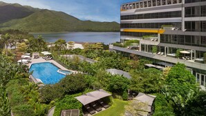 Un hotel moderno con piscina, abundante vegetación y montañas al fondo.