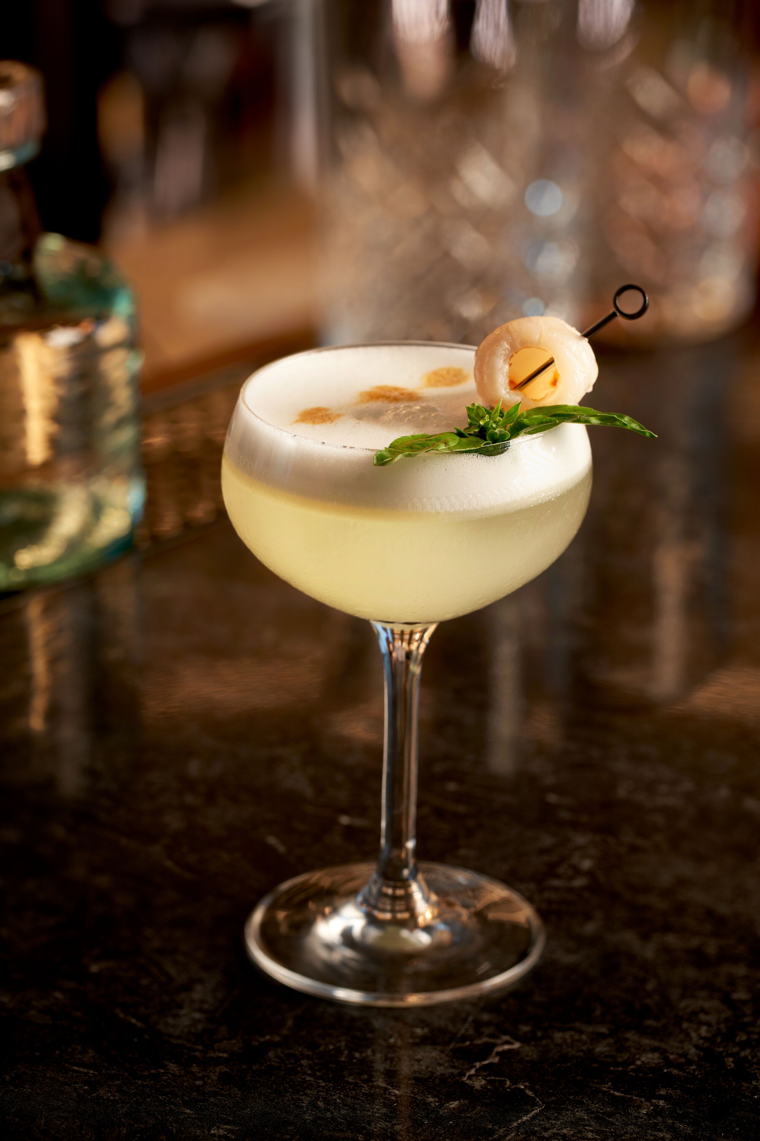 A cocktail in a coupe glass with a garnish, set on a bar counter.