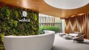 Zona de recepción con un mostrador blanco, una pared cubierta de plantas y mobiliario de mimbre.