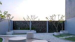 A modern outdoor area with a stone wall, potted plants, and circular seating. - Grand Omah Sastro (Depok)