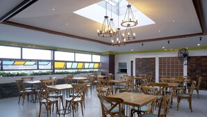 A spacious dining area with wooden tables and chairs, a skylight, and a decorative fan. - Grand Omah Sastro (Depok)