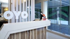 A reception desk with a large 'OYO' sign, a modern interior, and a view of the outside through large windows. - Grand Omah Sastro (Depok)