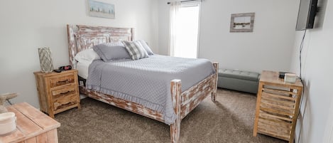 Un dormitorio con una cama de madera rústica, una mesita de noche, un aparador, un ventilador de techo, un televisor y una ventana con cortinas.