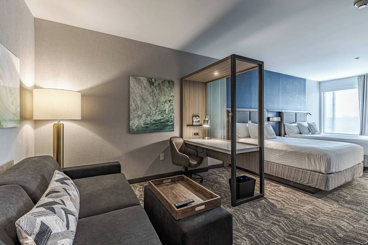 Una habitación de hotel con cama, escritorio, silla, sofá, lámpara, bandeja y un espejo grande.
