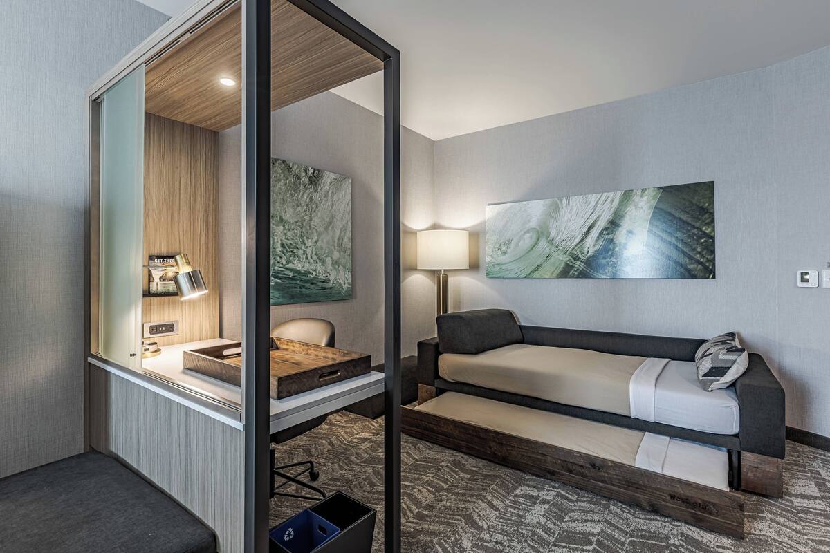 Una habitación de hotel compacta con escritorio, silla, sofá y obras de arte en las paredes.