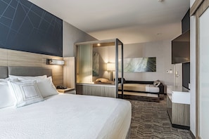 A modern hotel room with a large bed, a desk, a sofa, and a TV.