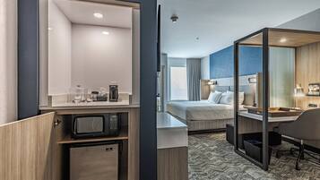 A hotel room with a bed, a desk, a microwave, and a small refrigerator.