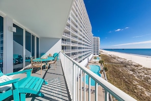 A balcony with turquoise chairs and a pool, overlooking a beach and a hotel building.