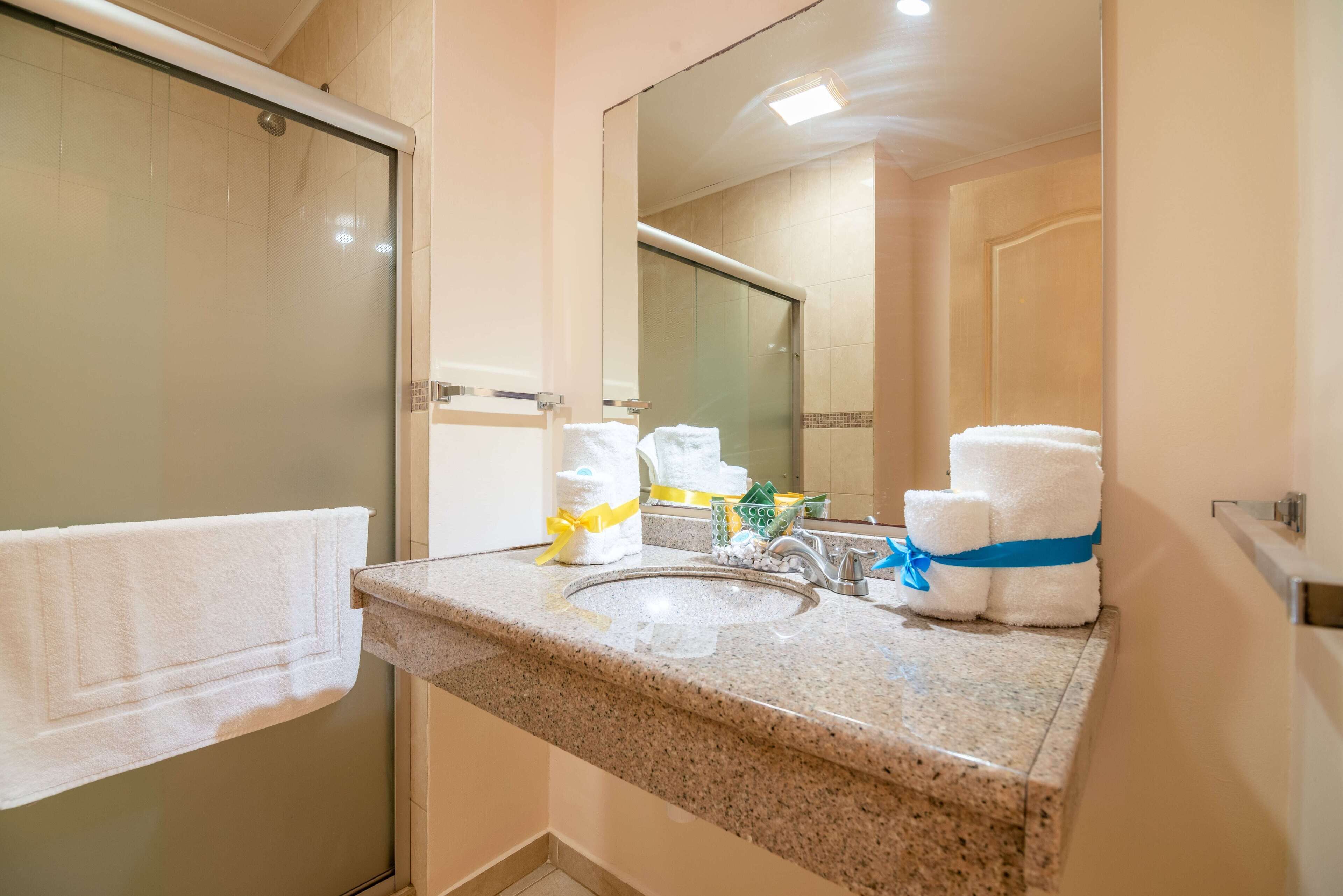 Une salle de bain avec un comptoir en granit, un lavabo et un miroir. On y trouve des serviettes et des articles de toilette sur le comptoir.