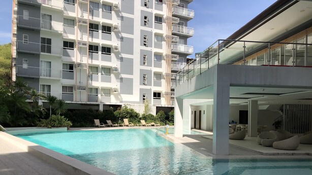 Un hotel moderno con piscina, sillones de descanso y un edificio de varios pisos con balcones.