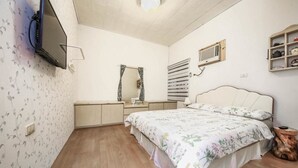 Un dormitori amb un llit, un televisor fixat a la paret, un mirall, una estant amb objectes decoratius i un terra de fusta.