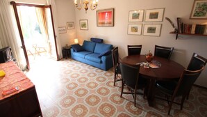 A dining area with a round wooden table and chairs, a blue sofa, and a chandelier. - Lake view Silvano Apartment (Baveno)