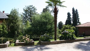 A garden with a palm tree, various shrubs, and a brick building. - Lake view Silvano Apartment (Baveno)