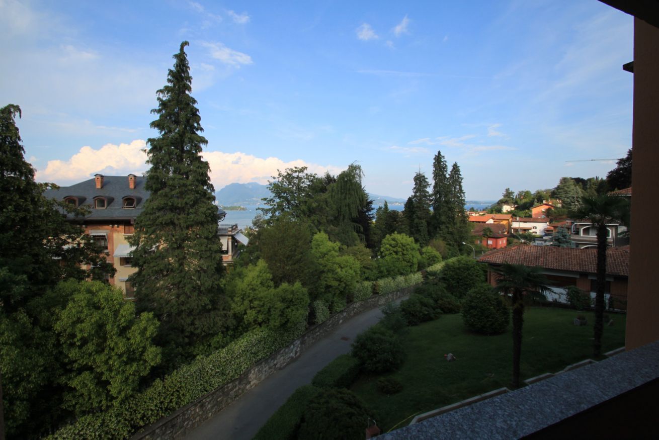 Ein Wohngebiet mit Blick auf einen See und Berge. Mehrere Häuser unterschiedlicher Architektur stechen hervor, umgeben von üppigem Grün und Bäumen.