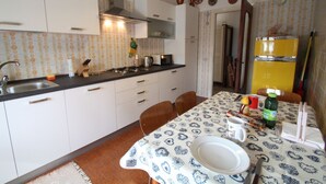 A kitchen with white cabinets, a stove, and a dining table set with plates and cutlery. - Lake view Silvano Apartment (Baveno)
