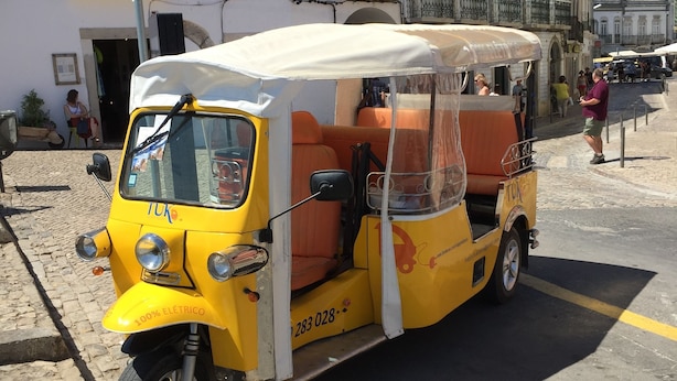 Un tuk-tuk amarillo estacionado en una calle empedrada.