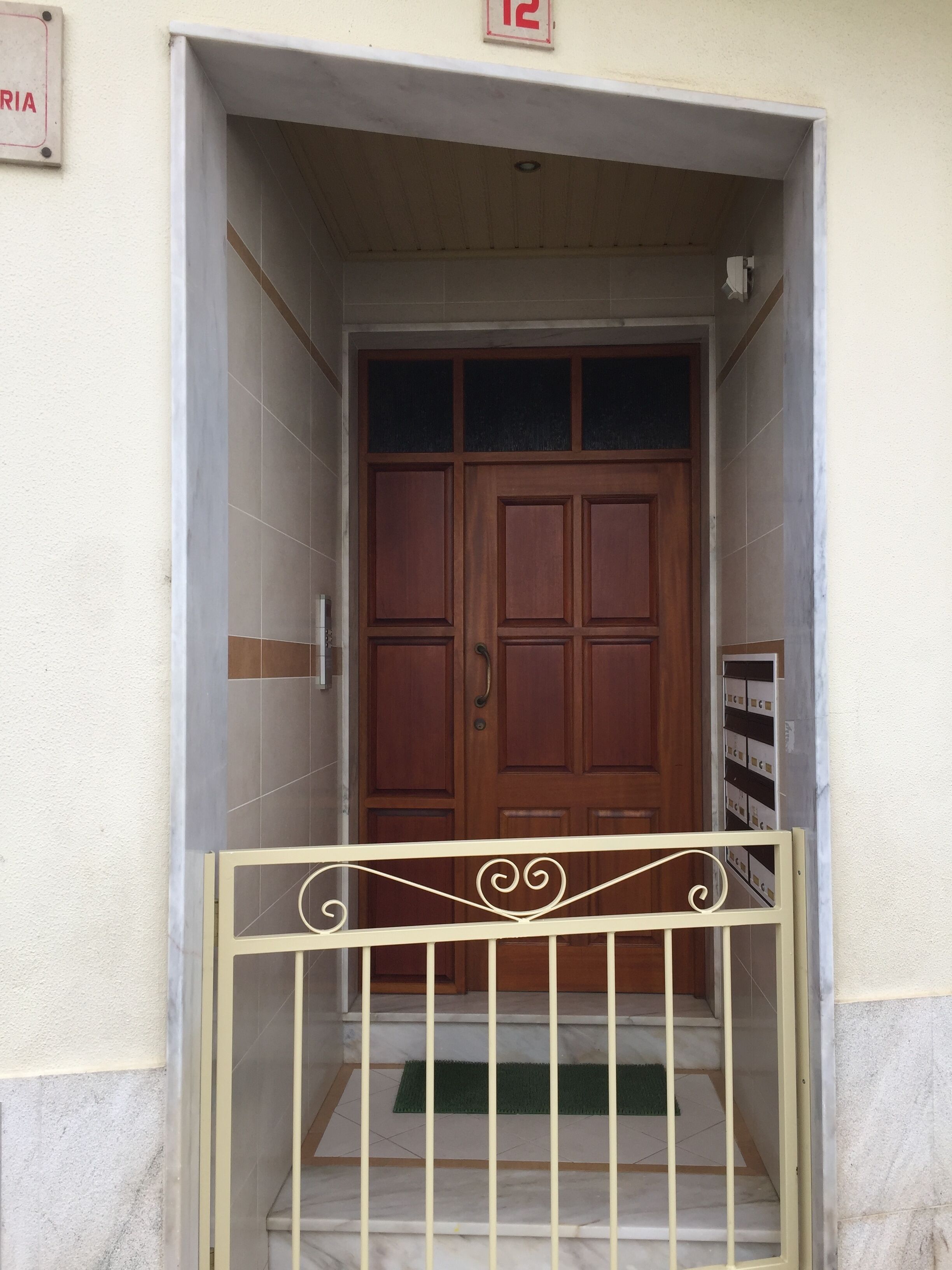 A wooden door with a metal gate in front, a tiled floor, and a small green mat at the entrance.