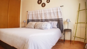 Una cama bien hecha con ropa de cama a rayas, un cabecero con cortina decorativa y una mesita de noche con lámpara.