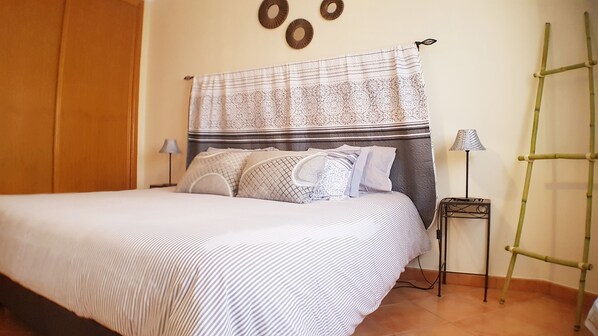 A neatly made bed with striped bedding, a headboard with a decorative curtain, and a bedside table with a lamp.