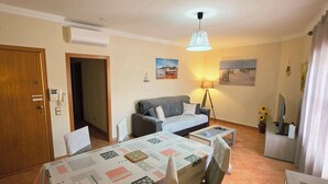 Una sala de estar con un sofá, una mesa de comedor con sillas, una lámpara y un televisor.